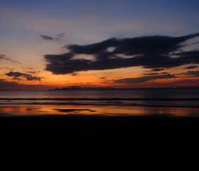 Obraz premium Sunset over the Andaman Sea from Tarutao Island, where soft sun rays illuminate the tranquil beach and distant islands.