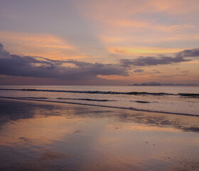 Sunset over the Andaman Sea from Tarutao Island, where soft sun rays illuminate the tranquil beach and distant islands.