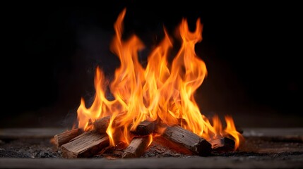 Fototapeta premium Intense orange flames flicker from a burning campfire made of logs against a dark background