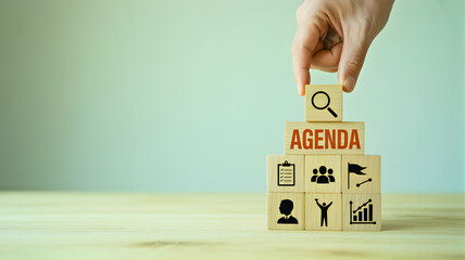 Hand arranging wooden blocks spelling 'AGENDA' with various business icons, symbolizing strategic planning, meeting organization, goal setting, and team collaboration for project success