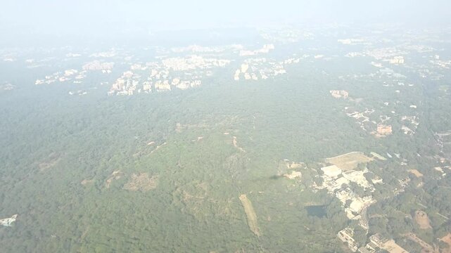 Aerial footage of green land with scattered buildings and forested areas seen from a flying airplane.