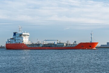 Fototapeta premium A striking photograph of an orange tanker navigating calm waters under a sky filled with soft clouds. Ideal for maritime themes or promotional use, showcasing the beauty of maritime industry.