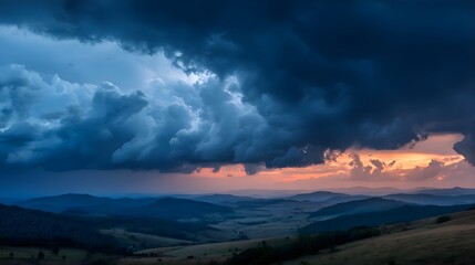 Dramatic stormy landscape with dark clouds and orange sunset over rolling hills and mountains