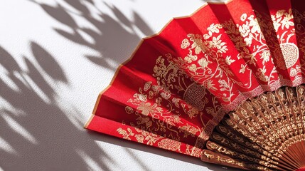 Red And Gold Folding Fan On White Surface With Leaf Shadows