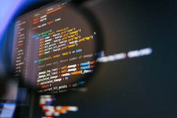 Colorful lines of code seen through a magnifying glass on a dark screen, symbolizing careful...
