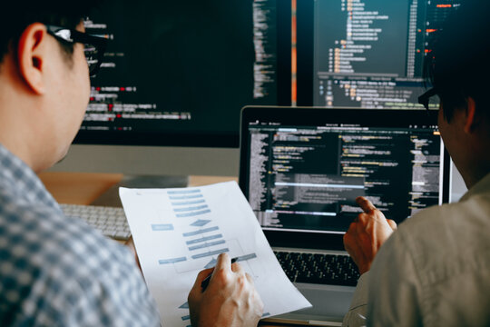 Two software engineers collaborating at a laptop filled with complex source code, reviewing printed documents and discussing key architecture decisions for an important development project

 - Powered by Adobe