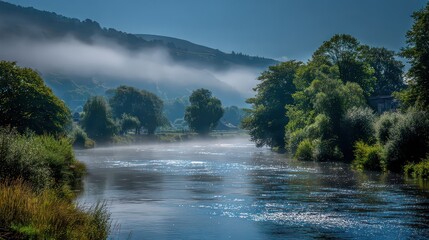 Scenic River Landscape with Fog Shrouded Hillsides Under Bright Sunlight Reflection Creates Glimmering Water Flowing Past Lush Green Trees And Bushes