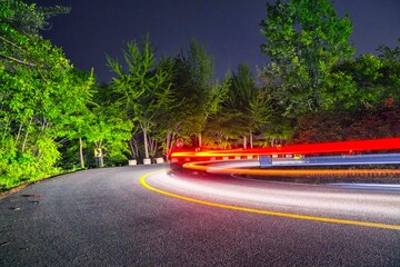 Long exposure of car light trails on a winding road at night with green trees © juwan