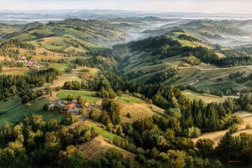 Naklejka premium A breathtaking aerial view of rolling green hills, dotted with trees and a quaint village, enveloped in morning mist under a clear blue sky.