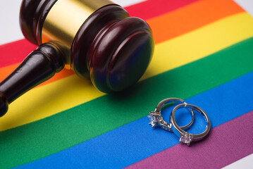 Close up wedding rings and judge wood gavel hammer on LGBT pride flag background with copy space. Legal status of same-sex marriage, LGBT human rights, equality and freedom concept.