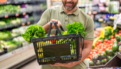 Man in grocery store. Man shopping with vegetable basket in supermarket. Grocery consumer. Man shopping at grocery store. Healthy lifestyle. Organic food basket. Grocery store checkout
