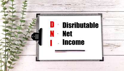 DNI acronym explained as distributable net income on clipboard with pen and green leaves on wood background
