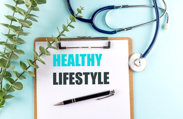 Healthy lifestyle concept on clipboard with stethoscope, pen and green leaves on blue background
