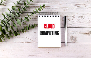 Cloud computing concept on notepad with silver pen and green leaves on wooden background