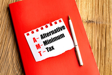 Alternative minimum tax written on torn paper on red notebook with pen on wooden table
