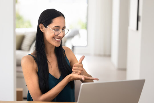 Happy young New Zealander woman speaking in sign language on video conference call at laptop, smiling, talking to people with hearing disability, deafness, caring for accessibility, inclusion