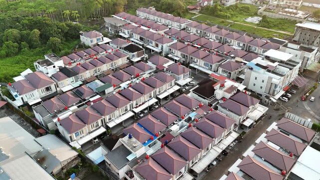 An aerial view showing rows of modern townhouses with red tile roofs, orderly streets, and surrounding green areas.