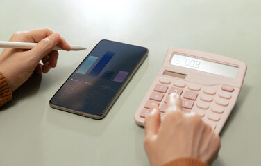 Hands using calculator beside smartphone with financial charts. Finance management
