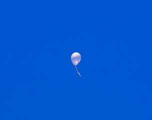 Low angle view of a single white balloon floating in the clear blue sky.
