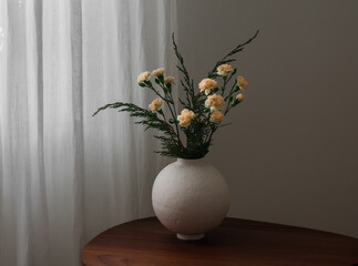 Yellow carnations, juniper branches, bouquet in a ceramic round vase on a wooden table