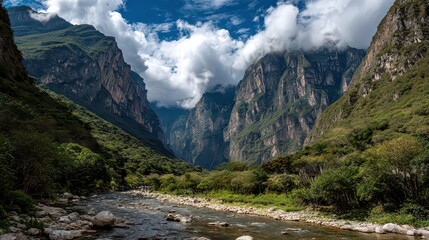 Obraz premium Green Mountain Valley with Flowing River Rocks and Dense Forest Under Blue Cloudy Sky on Sunny Day in Daylight