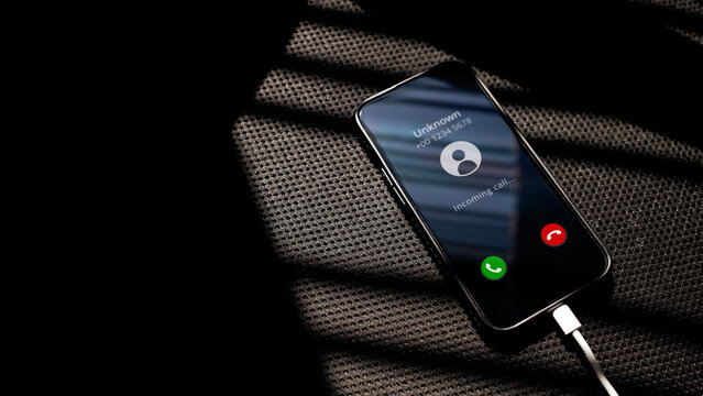 Unknown Incoming call on smartphone charging on a black chair textured surface. Communication and the use of mobile phones concept.
