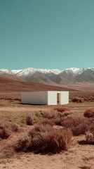 Minimalist White Rectangular Structure in Arid Landscape with Distant Snowy Mountains Under Clear Blue Sky Creates Contrast and Isolation