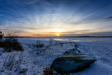 A boat on the shore of a frozen lake. A beautiful sunset