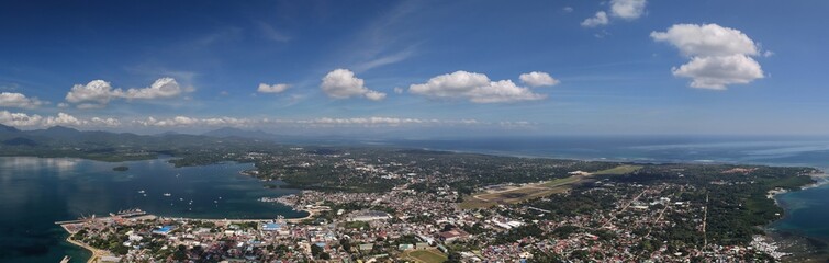 Obraz premium Expansive panoramic aerial photograph of Puerto Princesa City showcasing urban development, airport, coastal waters, and mountain backdrop in Palawan, Philippines.