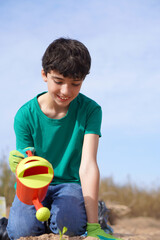 smiling child, planting a small plant and watering it with a watering can