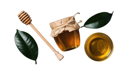 Honey jar with lid, dipper, dish with honey, and green leaves are displayed on a white surface no background