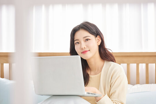 Young woman working on laptop in cozy bedroom.