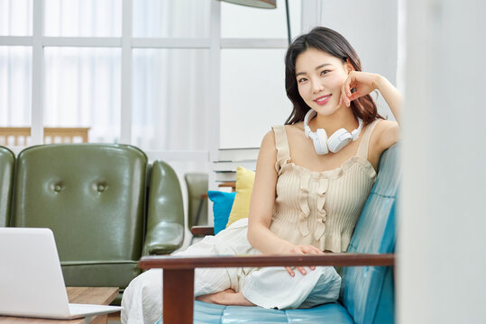 Relaxed young woman with wireless headphones on cozy sofa near laptop