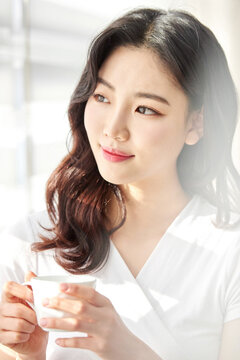 Young woman smiling while sipping from a white cup in sunny room