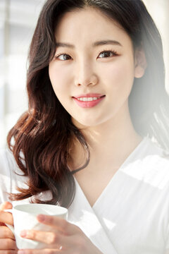 Young woman smiling while sipping from a white cup in sunny room
