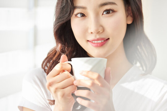Young woman smiling while sipping from a white cup in sunny room
