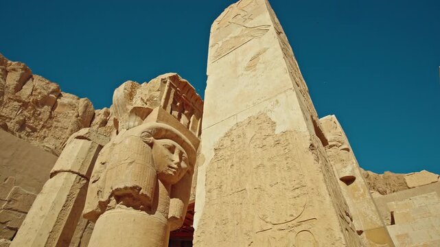 Low angle view of massive stone pillars and ancient statues at the Temple of Hatshepsut, carved into desert cliffs near Luxor
