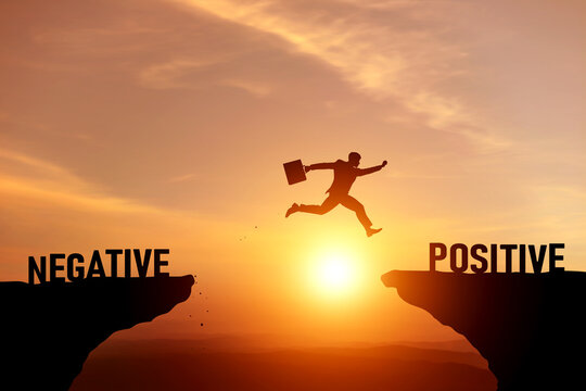 Silhouette of a businessman jumping over gap to change mindset from negative to positive. Concept of shifting perspectives and choose growth through a positive attitude for better chances of success.
