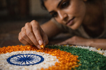 Close up of Indian woman artist carefully creating national flag rangoli with orange white and green flower petals on floor