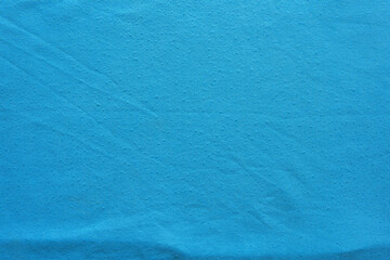 Close up of bright cyan blue textile material with subtle raised textured dots and slight wrinkles