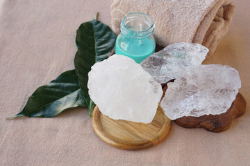 Natural alum stone spa still life with raw white and translucent alum crystals on wooden trays, green leaves, towel, and candle, representing natural deodorant, skincare, hygiene, wellness.