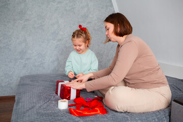 Side view of adult mother and her daughter pack a gift together for Valentine's Day and Mother's...