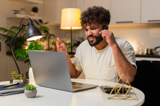 Arabian man at home wears headset answers hotline call types notes opens ticket gives info. Egyptian guy sitting at table listens repeats details confirms request records data schedules follow up