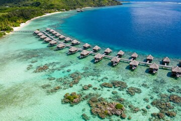 Aerial view of overwater bungalows on a tropical island with clear turquoise waters and coral reefs