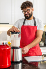 Arabian man blends milk whey protein banana apple smoothie for post workout recovery in kitchen at...
