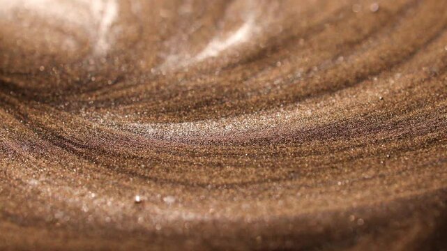 Mesmerizing shot of brush sweeping viscous golden paint, flowing horizontally and swirling slowly into curved, parallel texture ridges across frame.