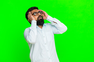 Indian man touches head with hand and looks tense, expressing emotional pressure, pain or inner stress. Arabian guy isolated on green chroma key background showing worry and mental discomfort reaction