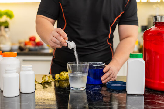 Sportsman pours scoop of supplement powder into glass of water in home kitchen. Concept of mixing electrolytes isotonic creatine glutamine bcaa slimming drink for fitness energy and muscle recovery.