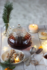 A transparent teapot with black tea on a wooden table. Sesame seed candies lie nearby.