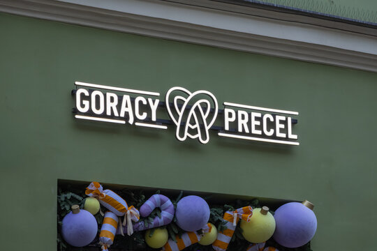 Krakow, Poland - December 1, 2025: Goracy Precel neon sign illuminates a green building facade, displaying a pretzel logo and festive holiday decorations